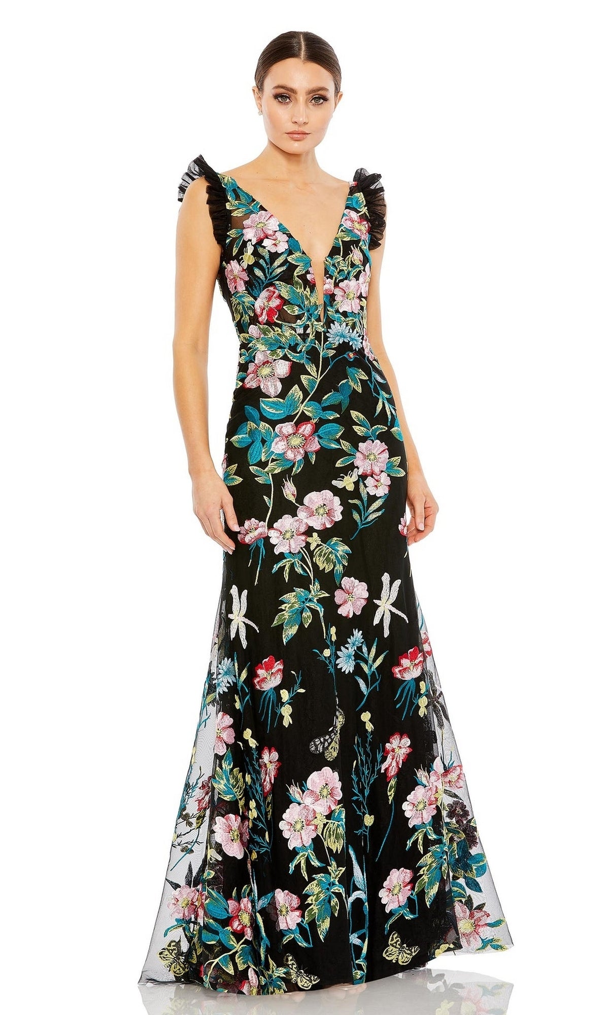 A woman models the Long Formal Dress 68273 by Mac Duggal, featuring a fitted silhouette, plunging v-neckline, and colorful floral embroidery, set against a plain white background.